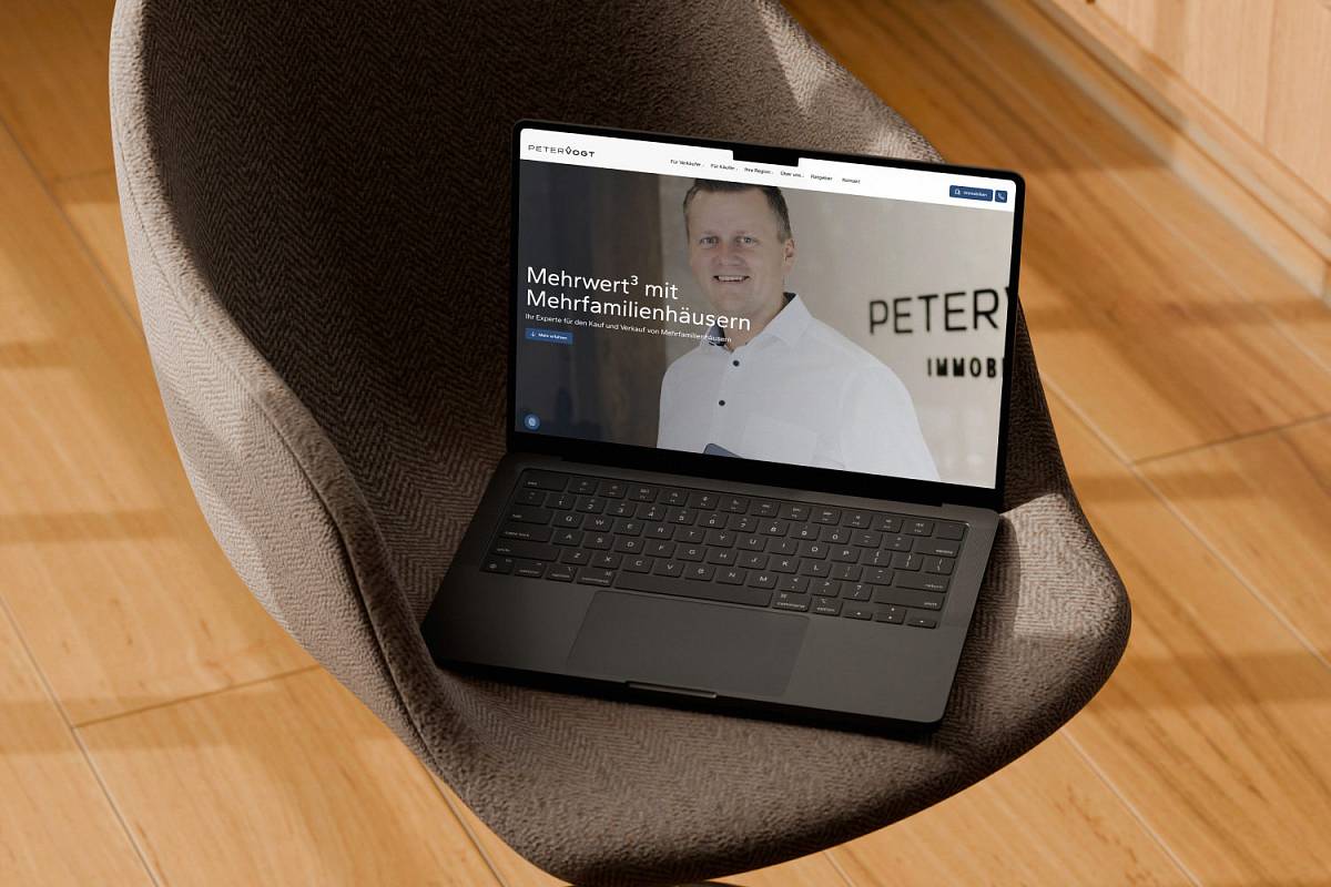 Laptop auf einem Polstersessel mit geöffneter Website eines Immobilienmaklers.